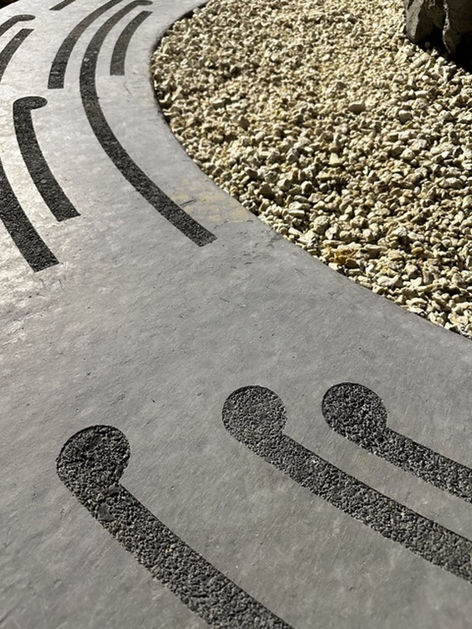 Portrait surface study, dark inlaid lines curving across grey stone and gravel