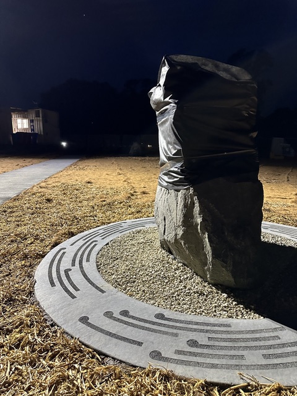 Standing carved stone work on its circular base, photographed at dusk